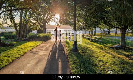 Un couple profitant du coucher de soleil dans un parc à Irvington, NY projette de longues ombres en se promenant vers la rivière Hudson Banque D'Images