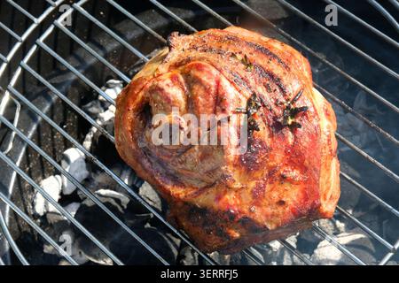 Un joint d'épaule non désossé d'agneau saisissant sur un barbecue à charbon de bois extérieur, assaisonné de romarin frais et d'herbes pendant le processus de cuisson. Banque D'Images