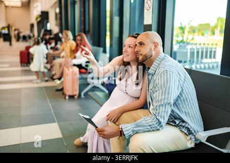 Couple attendant avec des cartes d'embarquement dans le salon des départs de l'aéroport pointant Banque D'Images