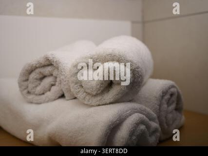 Une pile de serviettes en coton blanc propres et roulées placées soigneusement sur une étagère en bois dans une configuration de salle de bain moderne. Concept d'équipements frais. Banque D'Images