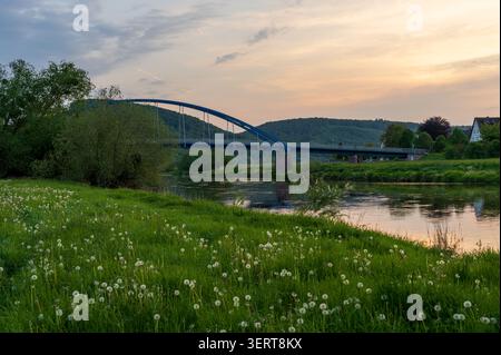 Golden Hour illumine les maisons traditionnelles le long de la rivière Weser, avec une eau tranquille reflétant la dernière lumière du jour et un pont menant à travers la rivière Banque D'Images