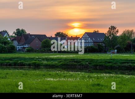 Golden Hour illumine les maisons traditionnelles le long de la rivière Weser, avec une eau tranquille reflétant la dernière lumière du jour. Banque D'Images