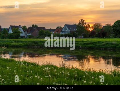 Golden Hour illumine les maisons traditionnelles le long de la rivière Weser, avec une eau tranquille reflétant la dernière lumière du jour. Banque D'Images