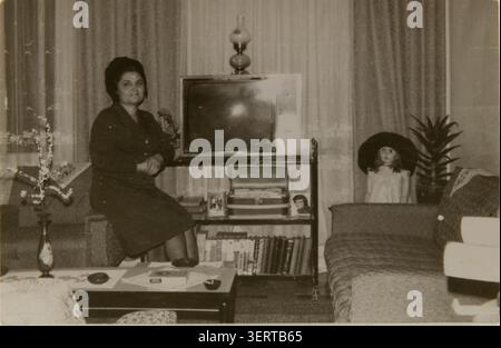 Izmir, Turquie - 19 juin 2026 : photo en noir et blanc d'une femme non identifiée posant à côté d'une vieille télévision à tube dans une maison turque des années 1970 avec une poupée étrange à droite et Banque D'Images