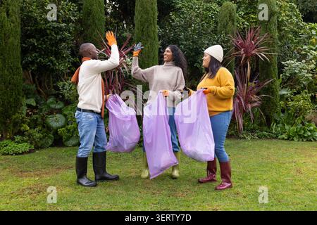 Divers bénévoles se sont élevés tout en collectant des sacs poubelles lilas dans le jardin avec des gants orange Banque D'Images