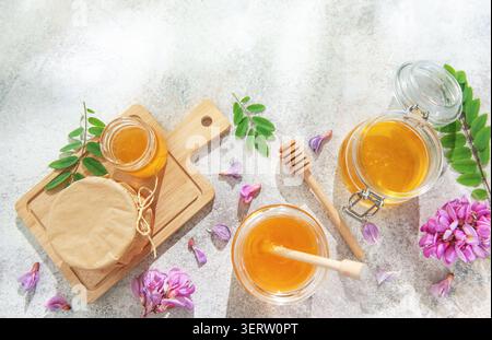 Pots de miel avec des trempettes, des fleurs d'acacia fraîches et des feuilles sur un fond clair Banque D'Images