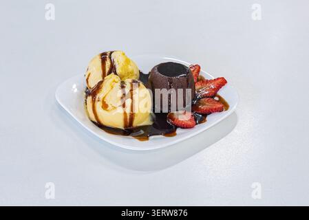 Studio shot avec gâteau à la lave servi avec des cuillères à glace à la vanille et des fraises fraîches sur une assiette blanche. Dessert arrosé de sirop de chocolat. SWE Banque D'Images