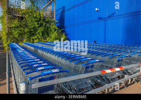 Kaarst, Allemagne, 10.06.2026 - rangées de chariots vides avec poignées bleues à l'extérieur d'un hypermarché, file d'attente de chariot en métal dans un parking de magasin contre Banque D'Images