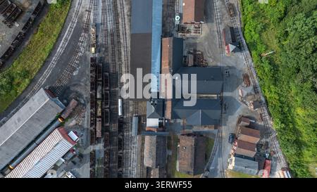 La scène montre une gare de triage avec plusieurs voies et divers bâtiments qui l'entourent. Plusieurs trains sont garés dans la cour. La zone est verte avec des arbres sur les bords. Banque D'Images