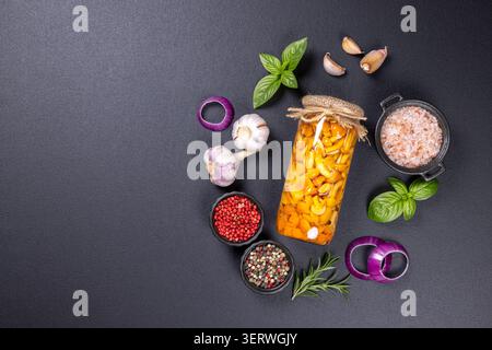 Champignons au miel marinés dans un bocal en verre. Entouré d'ail frais. Rondelles d'oignon rouge. Feuilles de basilic. Rosemary. Sel rose de l'himalaya. Et divers pepperco Banque D'Images