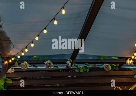 Ambiance chaleureuse en soirée avec guirlande lumineuse LED suspendue sur la terrasse du jardin. L'éclairage doux crée une atmosphère extérieure accueillante, Banque D'Images