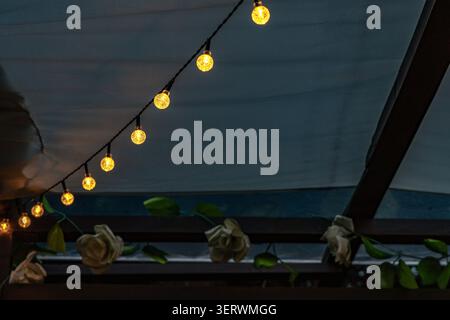 Ambiance chaleureuse en soirée avec guirlande lumineuse LED suspendue sur la terrasse du jardin. L'éclairage doux crée une atmosphère extérieure accueillante, Banque D'Images