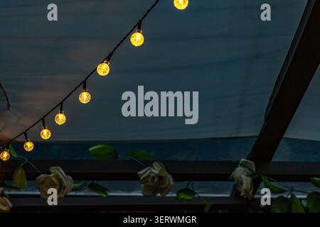 Ambiance chaleureuse en soirée avec guirlande lumineuse LED suspendue sur la terrasse du jardin. L'éclairage doux crée une atmosphère extérieure accueillante, Banque D'Images