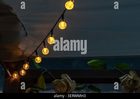Ambiance chaleureuse en soirée avec guirlande lumineuse LED suspendue sur la terrasse du jardin. L'éclairage doux crée une atmosphère extérieure accueillante, Banque D'Images