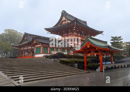 Kyoto, Japon - 10 avril 2026 : une geisha avec un unbrella sur un escalier du sanctuaire shinto Fushimi Inari-taisha sous la pluie Banque D'Images