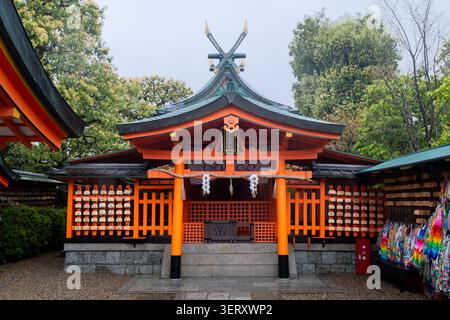 Kyoto, Japon - 10 avril 2026 : Ema Wood Wish plaques et bandes senbazuru sur un mur dans le sanctuaire shinto Fushimi Inari-taisha Banque D'Images