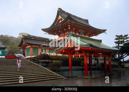 Kyoto, Japon - 10 avril 2026 : une geisha avec un unbrella sur un escalier du sanctuaire shinto Fushimi Inari-taisha sous la pluie Banque D'Images