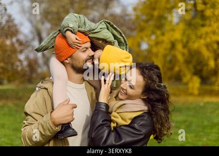 Parents amoureux embrassant leur fille sur les épaules lors d'une journée d'automne lumineuse à l'extérieur Banque D'Images