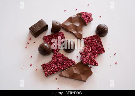 Chocolats cassés assortis avec framboises et bonbons au chocolat fourrés sur fond blanc Banque D'Images