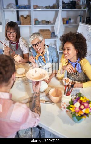 Professeur avec des élèves souriants peignant des pots en argile ensemble sur un atelier de poterie. Créatif, passe-temps, concept d'atelier Banque D'Images