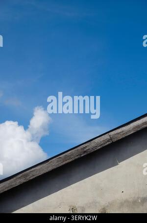Prise de vue à faible angle d'un vieux toit en bois altéré et d'un mur de béton sous un ciel bleu clair par une journée ensoleillée Banque D'Images
