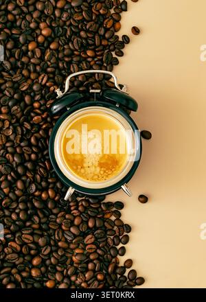 Tasse d'espresso frais intégré dans un réveil rétro entouré de grains de café sur fond beige. Concept de café créatif. Banque D'Images