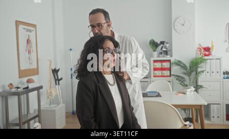 Le médecin place le stéthoscope sur la poitrine de la femme tout en écoutant dans le bureau médical du bâtiment, patient mi-âgé assis, médecin portant un manteau blanc et glasse Banque D'Images