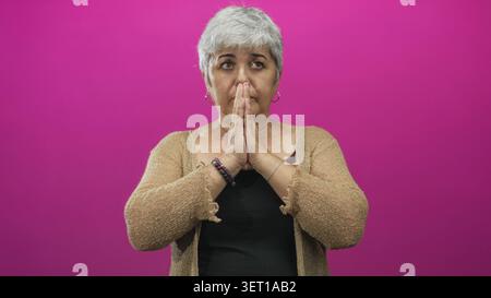 Femme âgée avec les paumes pressées ensemble dans le geste de prière et les yeux fermés dans le studio ; réflexion calme. Banque D'Images