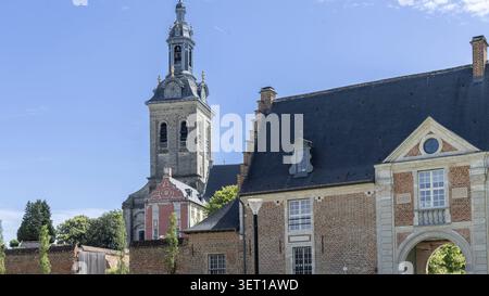 Le clocher de l'église historique d'Abdij van Park s'élève au-dessus des bâtiments en briques rouges à Louvain, en Belgique, encadrés par des arbres et un ciel bleu clair, mettant en évidence FL Banque D'Images