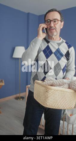 Homme au téléphone plaçant le lapin en peluche dans le panier à côté du berceau dans le bâtiment de la chambre de bébé ; organisation des soins. Banque D'Images