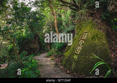 Rocher couvert de mousse avec une inscription chinoise à côté d’un sentier forestier sur le sentier de Xiangshan, Taipei, Taïwan. Banque D'Images