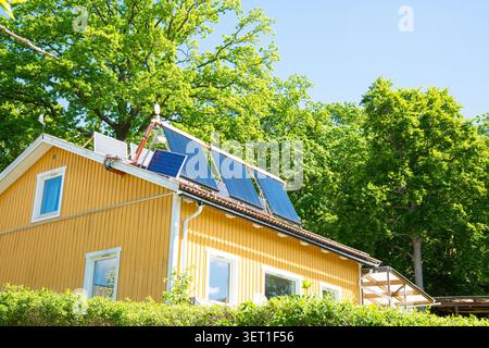 Maison jaune avec capteurs thermiques solaires et panneaux solaires sur le toit pour une énergie durable et le chauffage par une journée d'été ensoleillée Banque D'Images