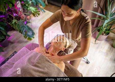 Femme détendue allongée sur la table de spa appréciant les procédures de routine de beauté dans la clinique cosmétique de luxe. Banque D'Images