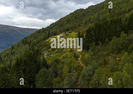 Vue aérienne de la ferme de montagne de Rakssetra avec des cabanes traditionnelles au toit en herbe sur une colline luxuriante entourée de forêt et de montagnes à Stryn Municipalit Banque D'Images