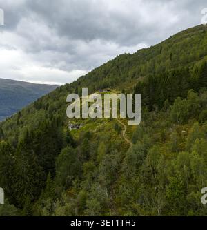 Vue aérienne de la ferme historique de montagne de Rakssetra avec des cabanes en bois, des pentes verdoyantes, des forêts de pins denses et un sentier de randonnée à Stryn Municipalit Banque D'Images
