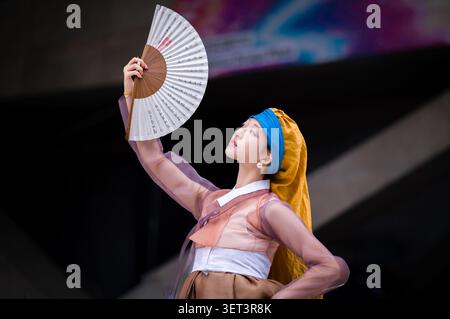 Une jeune femme asiatique portant un Hanbok coréen traditionnel et tenant un éventail de papier blanc ouvert, regardant vers le haut gracieusement. Banque D'Images