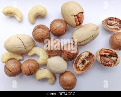 Vue de dessus arrangement de diverses noix comprenant des noix de macadamia entières et craquelées, des noix de pécan avec des noyaux visibles et des morceaux de noix de cajou dispersés sur un bri Banque D'Images