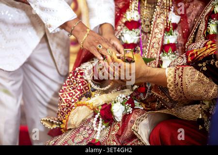 Gros plan des mains d'une mariée et d'un marié participant à un rituel sacré lors d'un mariage indien, orné de bijoux et de vêtements traditionnels Banque D'Images