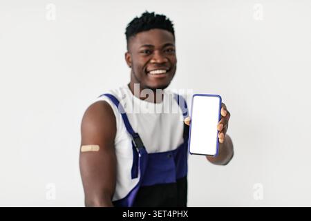 Joyeux Noir mâle montrant smartphone avec écran vierge, Studio. Concept technologique Banque D'Images