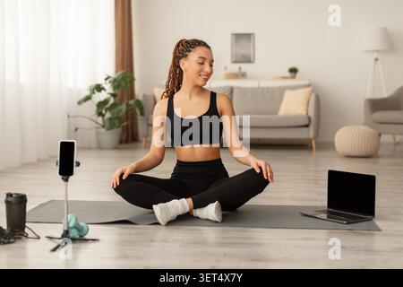 Sourire jeune femme noire méditant sur le tapis de yoga à la maison, concept Mindfulness Banque D'Images