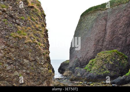 Vue spectaculaire à hauteur des yeux à travers d'imposantes falaises rocheuses et des formations de pierre côtières menant à la mer sur la côte d'Antrim. Banque D'Images