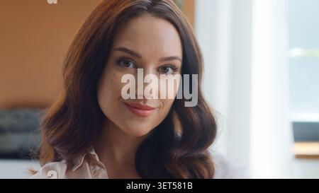 Gros plan sur le visage féminin attrayant. Mignonne femme d'affaires caucasienne souriante regardant la caméra femme d'affaires fille femme posant le sourire calme regardant à la maison Banque D'Images
