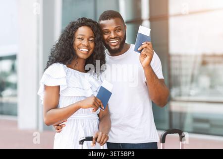 Couple heureux prêt pour le voyage à l'aéroport tenant des passeports et souriant dans un cadre lumineux Banque D'Images