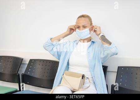 Femme portant un masque médical bleu, assise dans une salle d'attente, se concentrant sur la protection de la santé et les mesures de sécurité en attendant des soins médicaux Banque D'Images