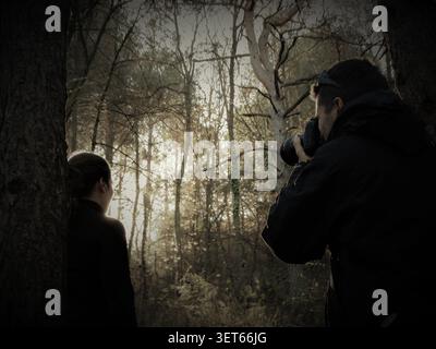 Photographe focalisant la caméra sur un modèle féminin debout dans une forêt sombre et atmosphérique Banque D'Images