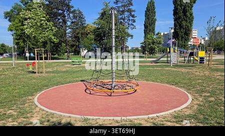 Un grimpeur de filet de corde conique vide avec un anneau de base orange se tient sur une zone de jeu caoutchoutée protectrice entourée de pelouses d'herbe et haut résidentiel Banque D'Images