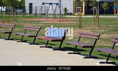 Un banc intelligent doté de panneaux photovoltaïques intégrés sur son dossier se dresse en ligne avec des lattes traditionnelles en bois brun assises à côté d'une pièce en plein air Banque D'Images