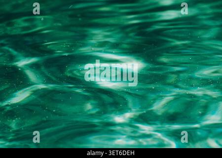 Surface de l'eau vert chatoyant avec de douces ondulations et des reflets de lumière dispersée créant une texture aquatique abstraite et tranquille Banque D'Images