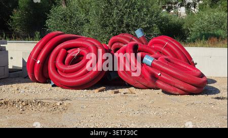 Un plan large capturant plusieurs rouleaux groupés de tuyaux ondulés rouges robustes utilisés pour les services publics souterrains et la protection des câbles électriques sur une tombe Banque D'Images