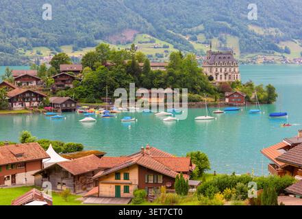 Village suisse traditionnel avec des maisons en bois et des bateaux amarrés sur la rive du lac de Brienz à Iseltwald, Suisse. Banque D'Images